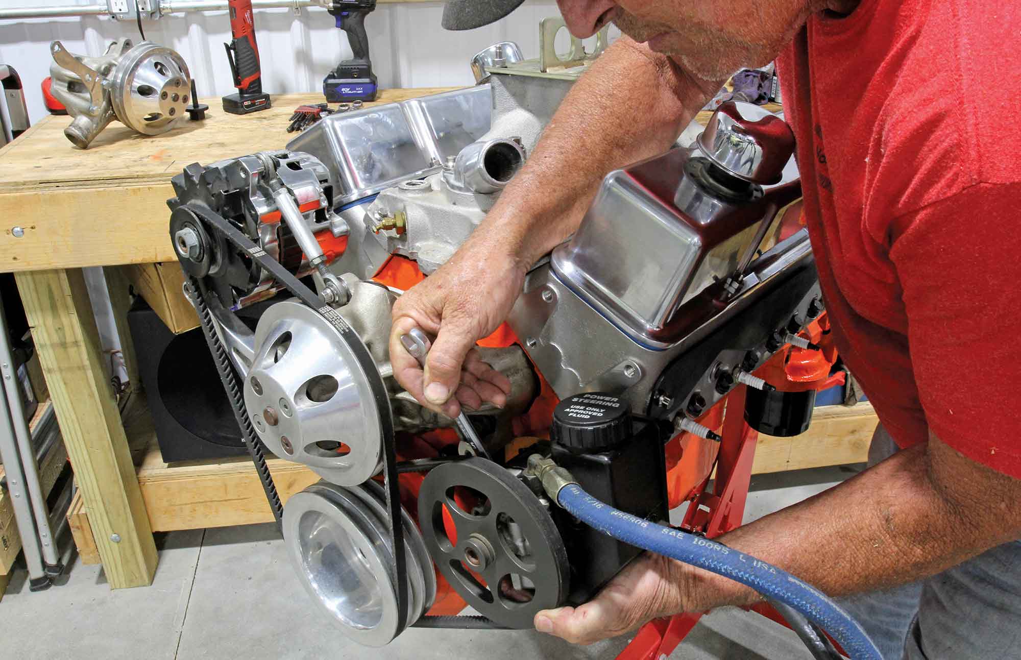 Mechanic working on a small-block Chevy engine's power steering pump.